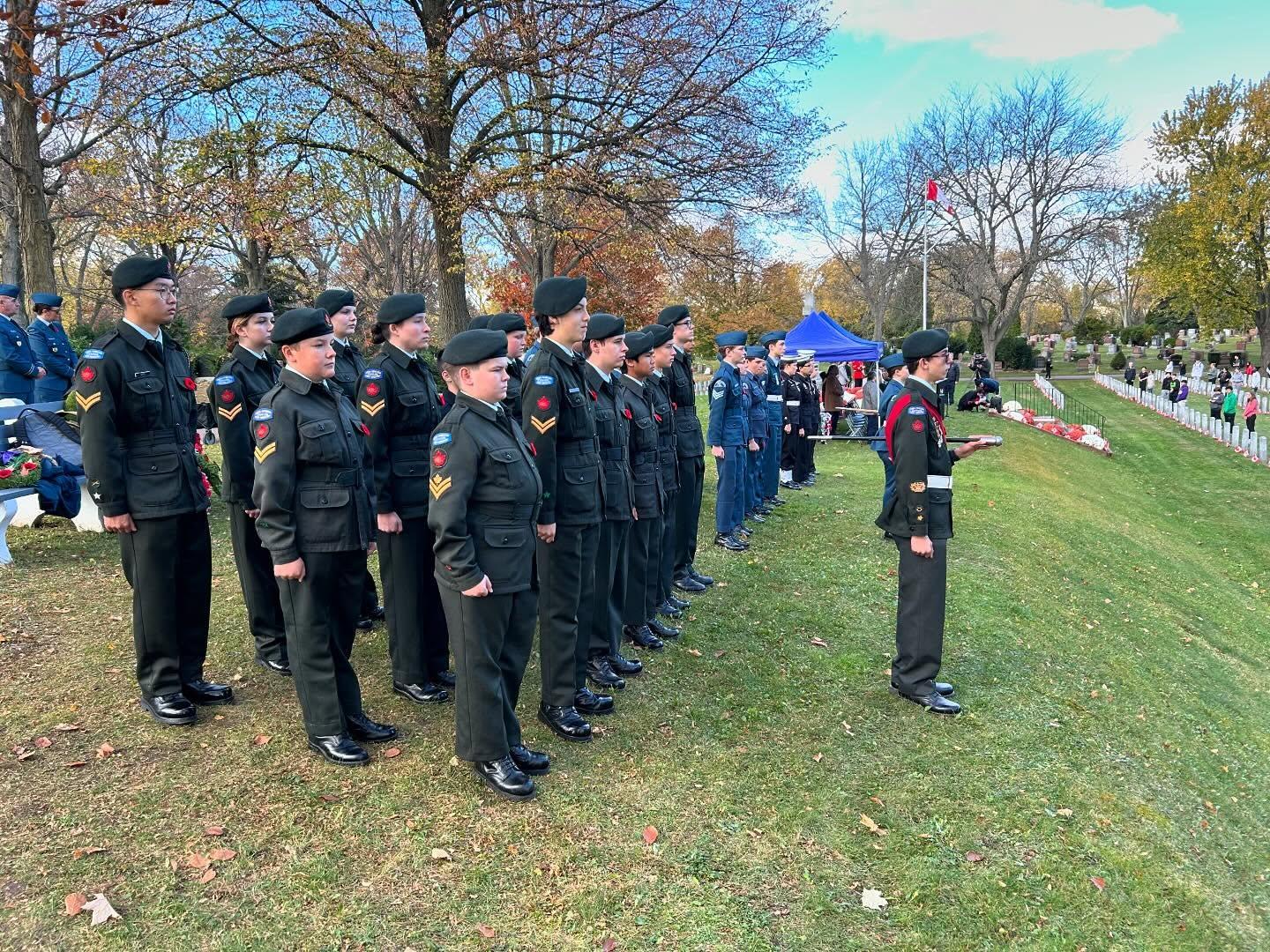 Wide view of attendees paying respects among rows of headstones on a clear autumn day