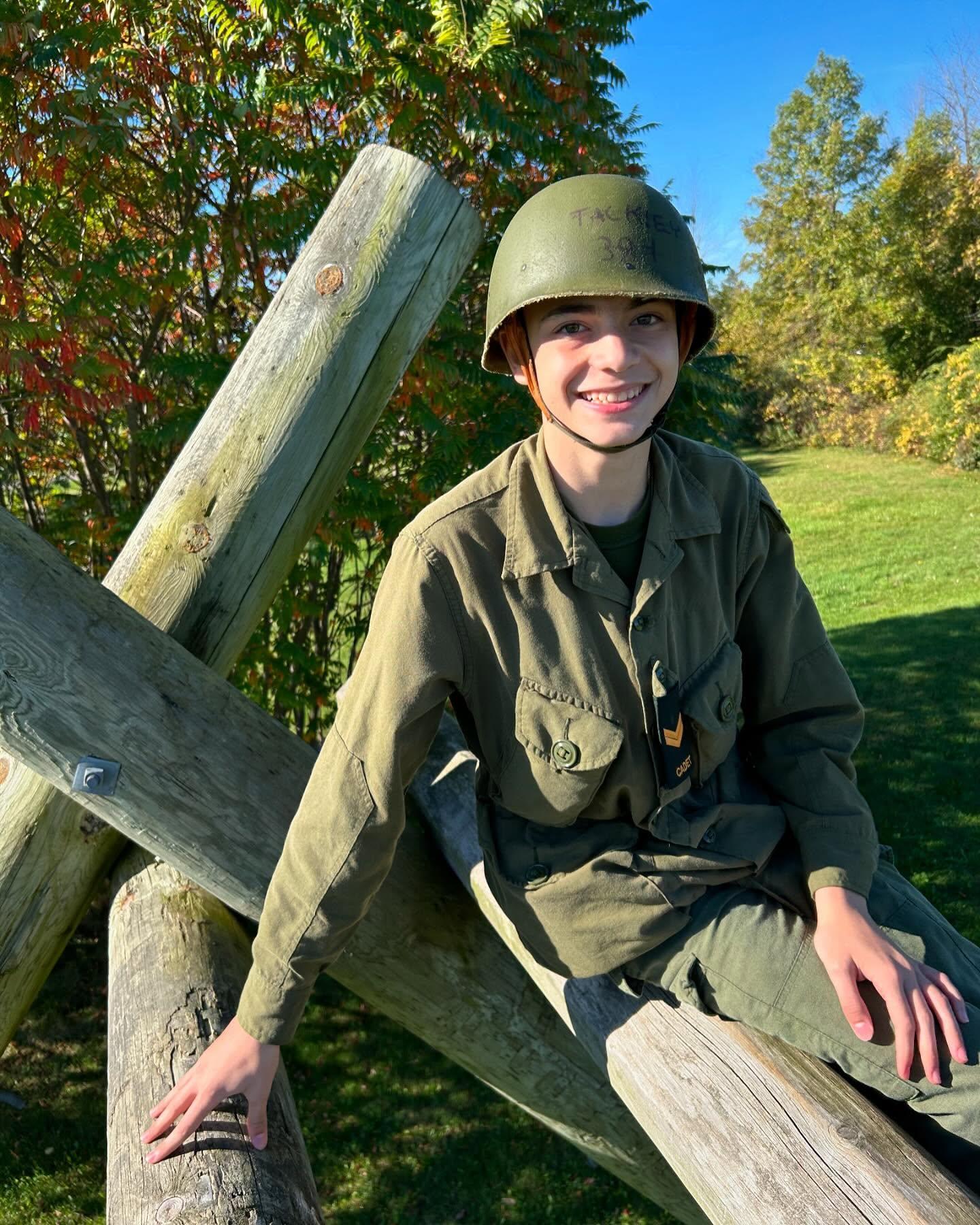 Cadet in camo helmet gripping the top of the wooden obstacle