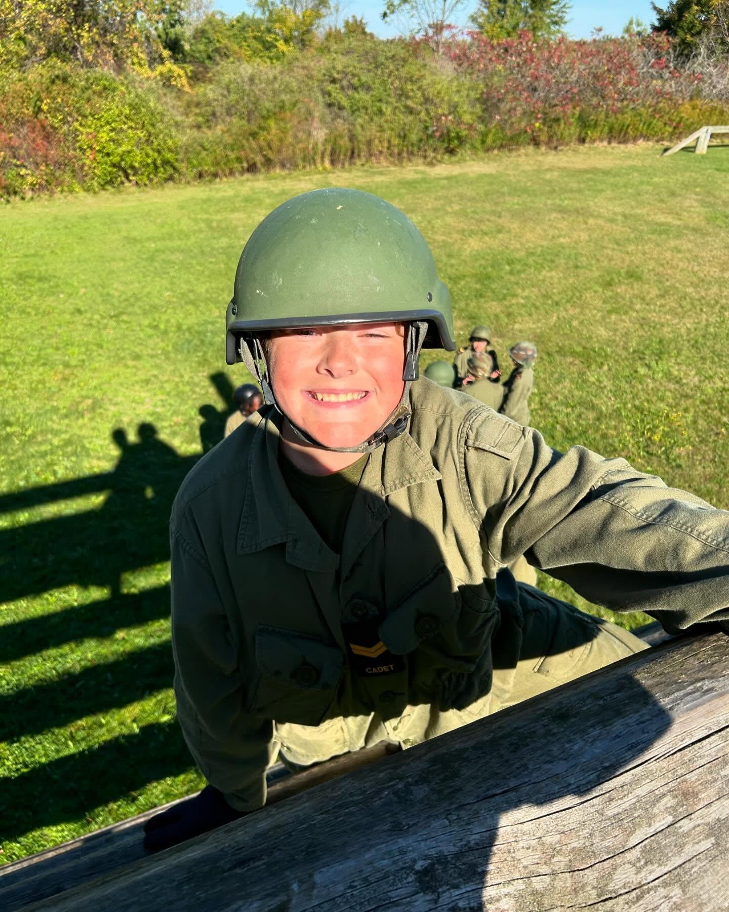 Cadet pulling themselves over a log obstacle with cadets watching below