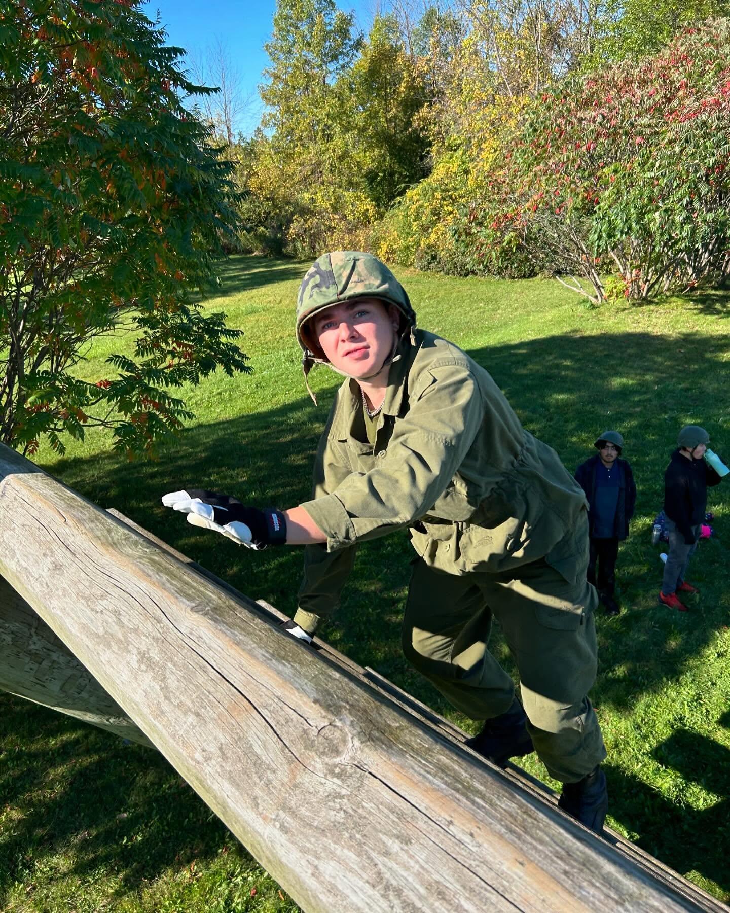 Cadet sitting on top of the obstacle course structure on a sunny day